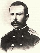 Un hombre adolescente con un bigote completo pero bien recortada, vestido con un uniforme naval oscuro