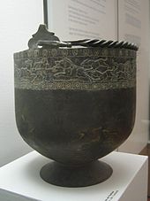 Cubo grande negro en forma de cuenco en un soporte. El cubo ha incrustación alrededor de su tapa.