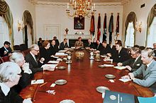 Thatcher es la única mujer en una habitación, donde una docena de hombres de traje se sientan alrededor de una mesa ovalada. Reagan y Thatcher se sientan uno frente al otro en el medio del eje largo de la mesa. La habitación está decorada en blanco, con cortinas, una araña de oro y un retrato de Lincoln.