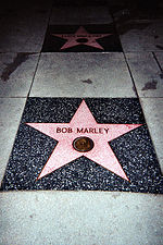 Un incrustaciones de estrella de cinco puntas de color rosa en la acera con Bob Marley escrito en él.