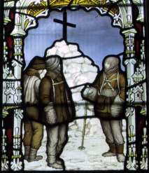 Tres figuras se representan en vidrio de color, de pie junto a un mojón de nieve coronada por una gran cruz. La escena está enmarcada por un arco decorativo.