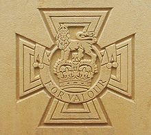 La cruz paté de oro que lleva la corona de San Eduardo coronada por un león con la inscripción al Valor grabado en piedra.