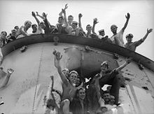 Close up de embudo de un barco, que tiene un gran agujero en el lado. Los marineros están sonriendo y saludando a los fotógrafos de la parte superior del embudo y el interior del agujero.