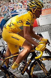 Un hombre en ropa de color amarillo, con un casco amarillo y handgloves amarillas, andar en bicicleta. Justo detrás de él es otro ciclista, en ropa azul.