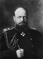 Un homme trapu, chauve avec une barbe, vêtu d'un uniforme militaire noir.