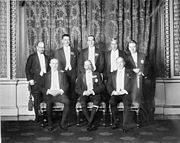 Un groupe pose de huit hommes en tenues de soirée intelligente. Le roi se trouve au milieu entouré de ses premiers ministres.