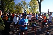 Trois femmes, deux souriant, et un homme avec sa main pointant en l'air la tête d'un grand groupe de coureurs lac Calhoun et certains observateurs passé