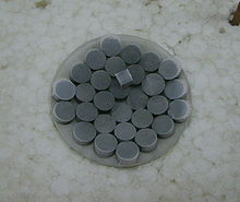 Pilules gris foncé sur un verre de montre. Une pièce cubique du même matériau au-dessus de la pilule.