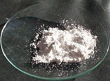 Verre de montre sur une surface noire avec une petite portion de poudre blanche