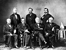 Sept hommes portant des costumes posant pour une photo de groupe.