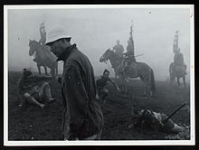 Kurosawa, un homme grand et mince à l'âge mûr tôt tourné vers la gauche, porter des vêtements modernes surmonté d'un bonnet blanc doux, promenades à travers un paysage brumeux, que derrière lui divers acteurs médiévale costume japonais apparaissent à cheval ou couchée ou assise sur le sol.