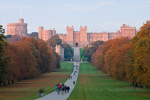 Un château de couleur rouge avec des créneaux et de tours réside dans la distance de la photographie. A courbes de chemin depuis le bas de l'image vers elle, avec diverses personnes flânant le long de lui. De chaque côté de l'herbe est plat et de bois verts.