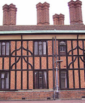 Une photographie en gros plan d'un bâtiment en bois avec des noirs et rouge brique. Le bâtiment a quatre grands, les cheminées de briques. Un tuyau d'évacuation relativement moderne descend au milieu du bâtiment.