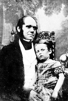 Darwin dans la trentaine, avec son fils habillé dans une robe assis sur son genou.