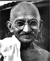 Le visage de Gandhi dans la vieillesse souriant, portant des lunettes, et avec une écharpe blanche sur son épaule droite