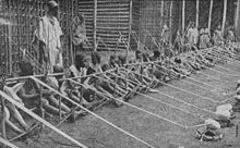 Une rangée de plus d'une douzaine d'enfants tenant des métiers en bois se étend dans la distance.