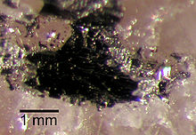 Une masse sombre, à environ 2 millimètres de diamètre, sur un substrat de cristal de couleur rose