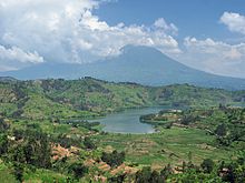 Photo d'un lac avec une des montagnes des Virunga derrière, partiellement dans les nuages