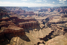 Grand canyon avec abruptes parois de couleur beige. Une rivière dans une vallée est sous une surface en pente douce large.