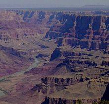 Une rivière de couleur grisâtre avec de la végétation verte sur ses banques, mais faible par rapport à la haute rougeâtre et murs ocre du canyon il se trouve.