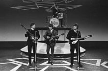 Image monochrome des Beatles effectuer sur une scène portant des costumes sombres.