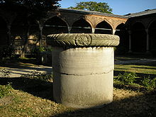 Une colonne solide cylindrique dans une cour devant arches palais de style islamique