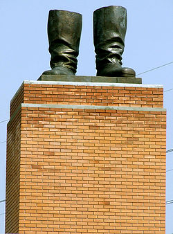 une brique piédestal tan supportant une paire de bottes statue de bronze avec rien attaché