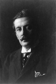 Tête et des épaules portrait dans l'ombre lourde, représentant un homme aux cheveux bruns avec une moustache de curling, portant un collier ailes avec une cravate et avec un mouchoir dépassant de la poche supérieure