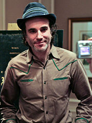 Un homme souriant coiffé d'un chapeau gris avec passepoil dessus de la bande, et une chemise de style occidental tan, se trouve dans un bureau, posant pour la caméra.