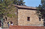 Photo d'un bâtiment de pierre brute avec de petites fenêtres, entourée d'oliviers.