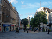 Zona comercial Fargate, Sheffield. Uma vez que uma estrada movimentada, foi para peões por várias décadas e é a principal área de compras Centro da Cidade de Sheffield, o lar de muitas empresas bem conhecidas. A imagem mostra a arquitetura clássica em ambos os lados com um plano de espaços no centro, pontilhada com árvores e as construções na High Street são visíveis além das árvores.