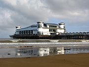 Uma passagem suportado por pernas de metal resultantes do mar, no final dos quais é um grande edifício branco com um telhado em forma de onda e de canto torres.
