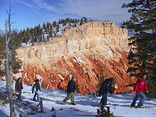 Uma linha de snowshoers com penhasco rocha colorida no fundo.
