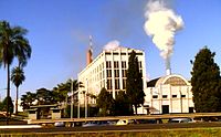 Foto do edifício mais curto, com fumaça saindo da chaminé ao lado de cinco andares edifício de escritórios