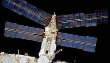 Uma vista do módulo Spektr com a escuridão do espaço por trás. Em vista são quatro painéis solares de ouro do módulo, para além do próprio módulo cilíndrico, coberto de isolamento branco e com um cone na extremidade distai do módulo. Duas das matrizes projectar a partir deste cone, e duas projecto a partir da extremidade distal do cilindro.