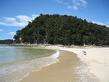 Foto que mostra a água azul claro, um fotógrafo ou turista captar a água em uma praia dourada areia e colinas arborizadas