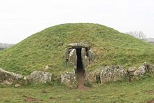 Um baixo monte gramíneo com uma entrada em seu centro emoldurado por pedras ciclópicas