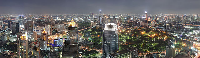 Fotografia panorama em tempo noite que mostra uma paisagem expansiva com vários arranha-céus em primeiro plano, a um parque no centro, e um grande grupo de edifícios em todo o parque