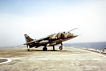 A Harrier sobre o convés de um pequeno porta-aviões, com sua roda de nariz fora do baralho