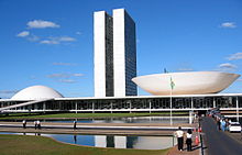 A exibição mostra um edifício do século 20 com duas torres idênticas muito próximos uns dos outros dois subindo de um edifício baixo que tem uma cúpula em uma extremidade, e uma cúpula invertida, como um disco, no outro.