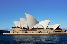O Sydney Opera House parece flutuar no porto. Tem numerosos telhado secções que são em forma de grandes velas brancas brilhantes