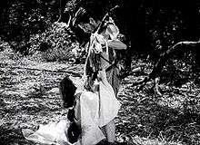 Uma foto de dois atores, Toshiro Mifune e Machiko Kyo, dentro de uma floresta, em uma cena do filme japonês de 1950, Rashomon: Ms. Kyo, uma mulher jovem e atraente, é visto em um período do século 11 quimono à esquerda do quadro, ajoelhando-se aos pés de Mifune; Mifune, na direita do quadro, vestindo o traje áspero de um bandido desse período, está olhando para Ms. Kyo como ela aparece para pleitear com ele.