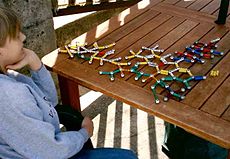 Menino sentado de frente para 3/4 longe da câmera, olhando para um modelo da bola-e-vara de uma estrutura molecular. O modelo é feito de ímãs coloridos e bolas de aço.