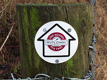 Borne de madeira com waymarker circular que mostra uma seta que contém o logotipo de Butcombe Brewery