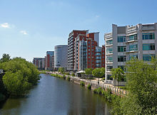 O rio Aire canalizado flui dos Arcos escuras sob principal estação ferroviária de Leeds para a parte inferior da imagem. À esquerda do rio é o bloqueio que liga o rio com o Leeds e Liverpool Canal. Para a direita é um passeio ribeirinho sob edifícios modernos, e à distância, além do viaduto ferroviário e da estação, são mais de arranha-céus modernos edifícios localizados no lado oeste do centro da cidade.