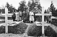 17 homens, a maioria em uniforme militar, ficar em um cemitério, vendo duas sepulturas.