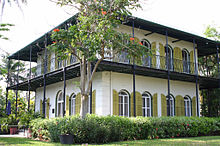 casa quadrada de dois andares, com janelas altas e persianas exteriores e uma varanda do segundo andar