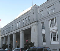 Fachada de um grande edifício branco, o deixou ter grandes pilares debaixo de uma tira com dezenas de janelas e os três certas histórias de grandes janelas.