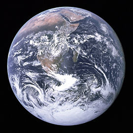 Um disco planetário de formações de nuvens brancas, marrons e verdes massas de terra e oceanos azuis escuros contra um fundo preto. A península da Arábia, África e Madagáscar encontram-se na metade superior do disco, enquanto a Antártida é na parte inferior.