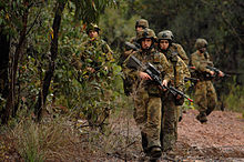 Um grupo de soldados australianos com rifles se movendo ao longo de um trajeto em uma área arborizada
